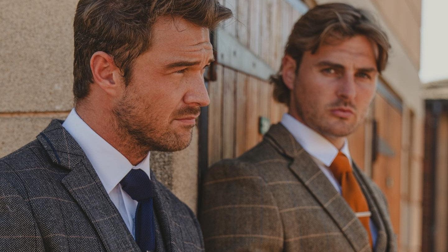 Two men in Cavani tweed suits standing side by side against a building.