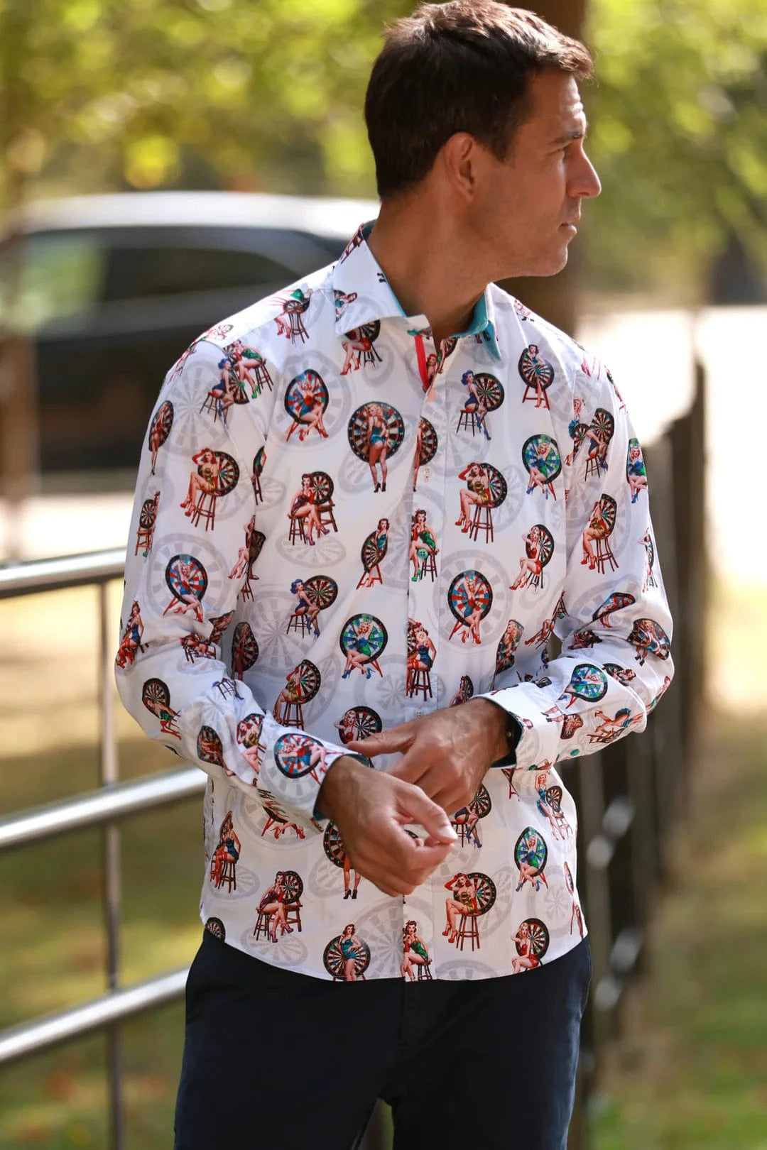 A man wearing a Claudio Lugli dartboard pin-up print shirt with a colorful pattern, displaying classic pin-up girls and dartboards.