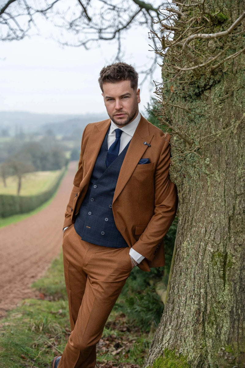 Man in a brown suit standing next to a tree with a scenic background