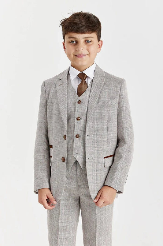 Young boy wearing a beige checkered suit with a white shirt and brown tie on a light gray background