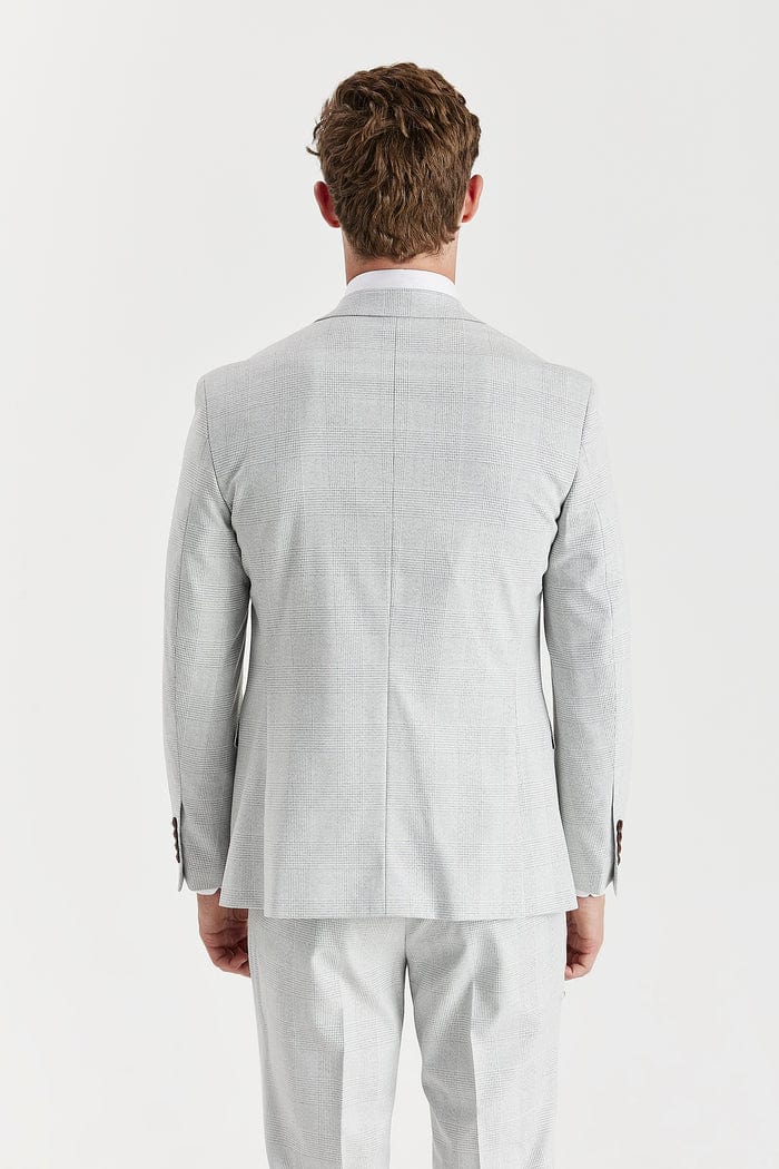 Man wearing a Paul Andrew stone check suit with a white shirt and brown shoes on a white background