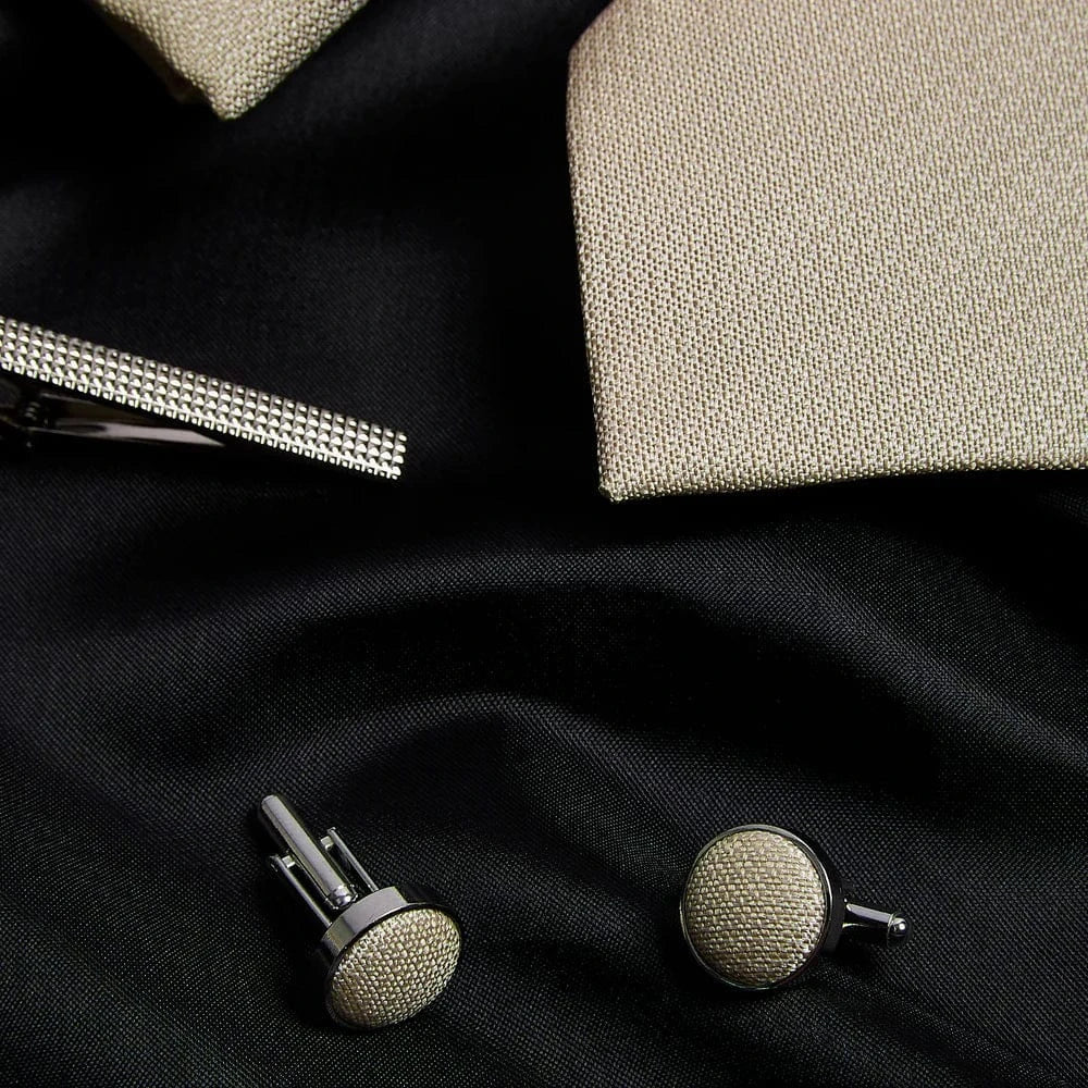Cufflinks on a black fabric background with a tie and tie clip.