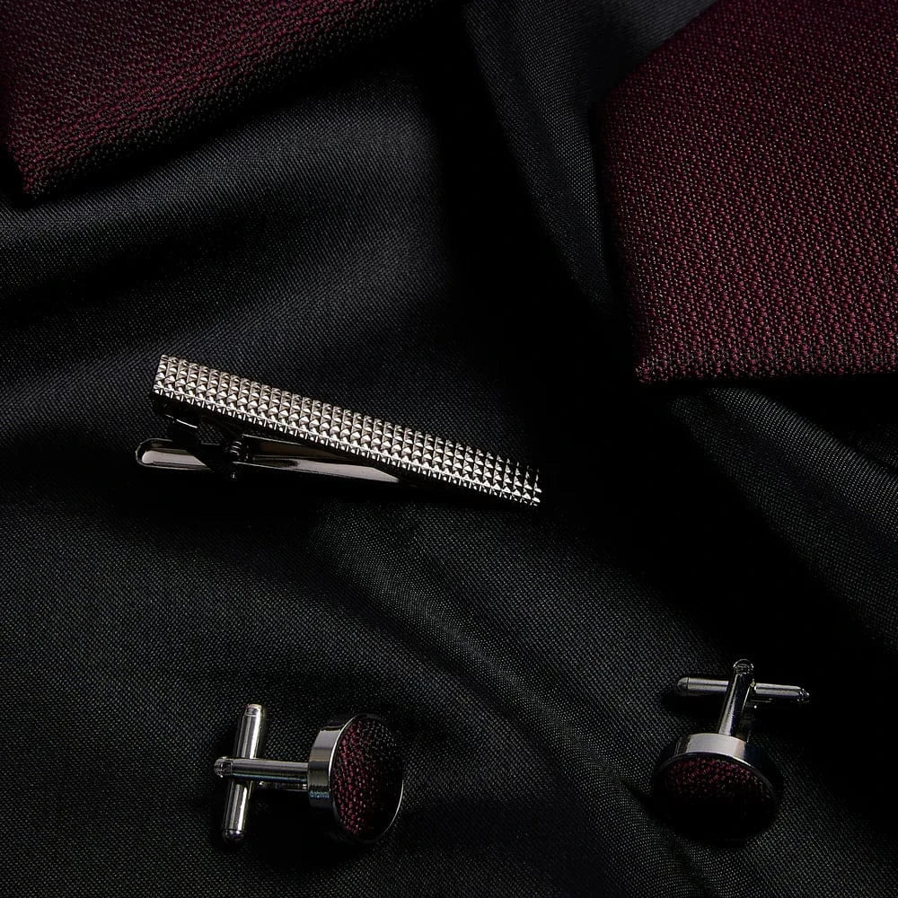 Silver tie clip and cufflinks on a black fabric background