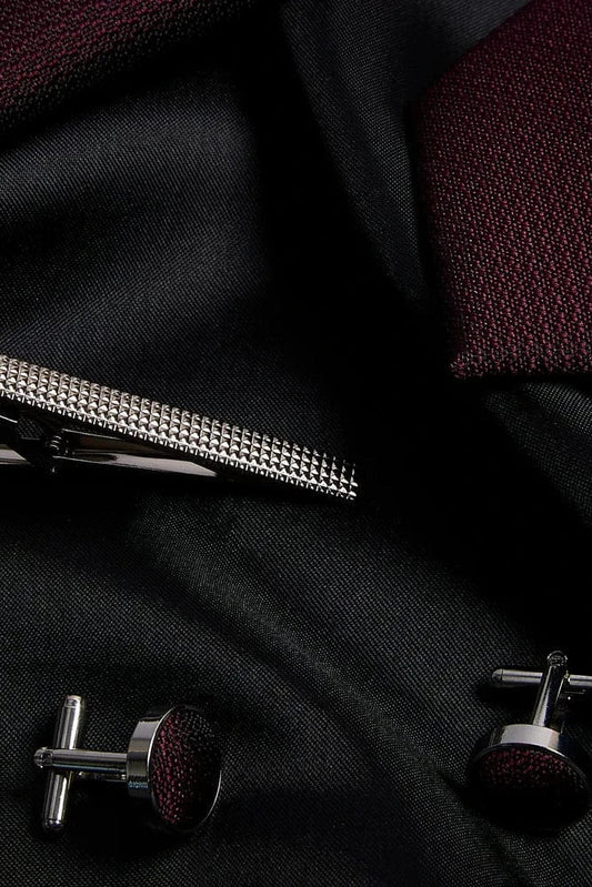 Silver tie clip and cufflinks on a black fabric background