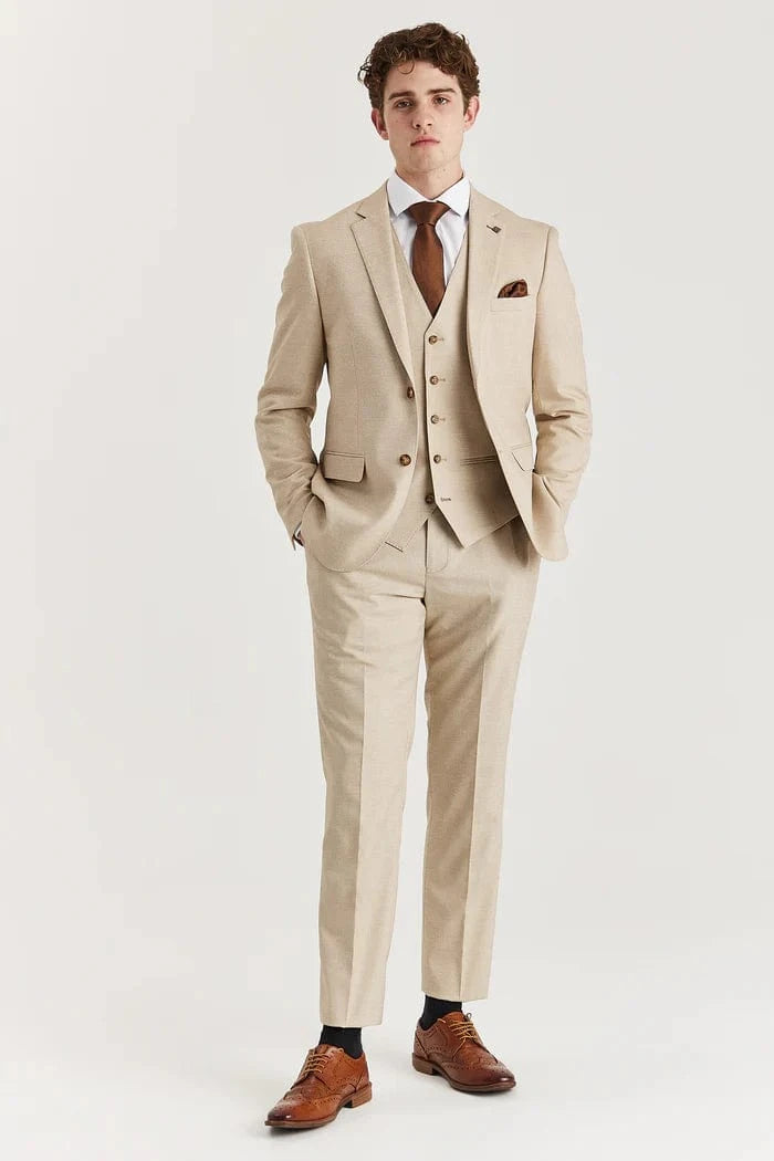 A male model wearing a beige three-piece suit with a waistcoat and trousers, paired with a white shirt and brown shoes.