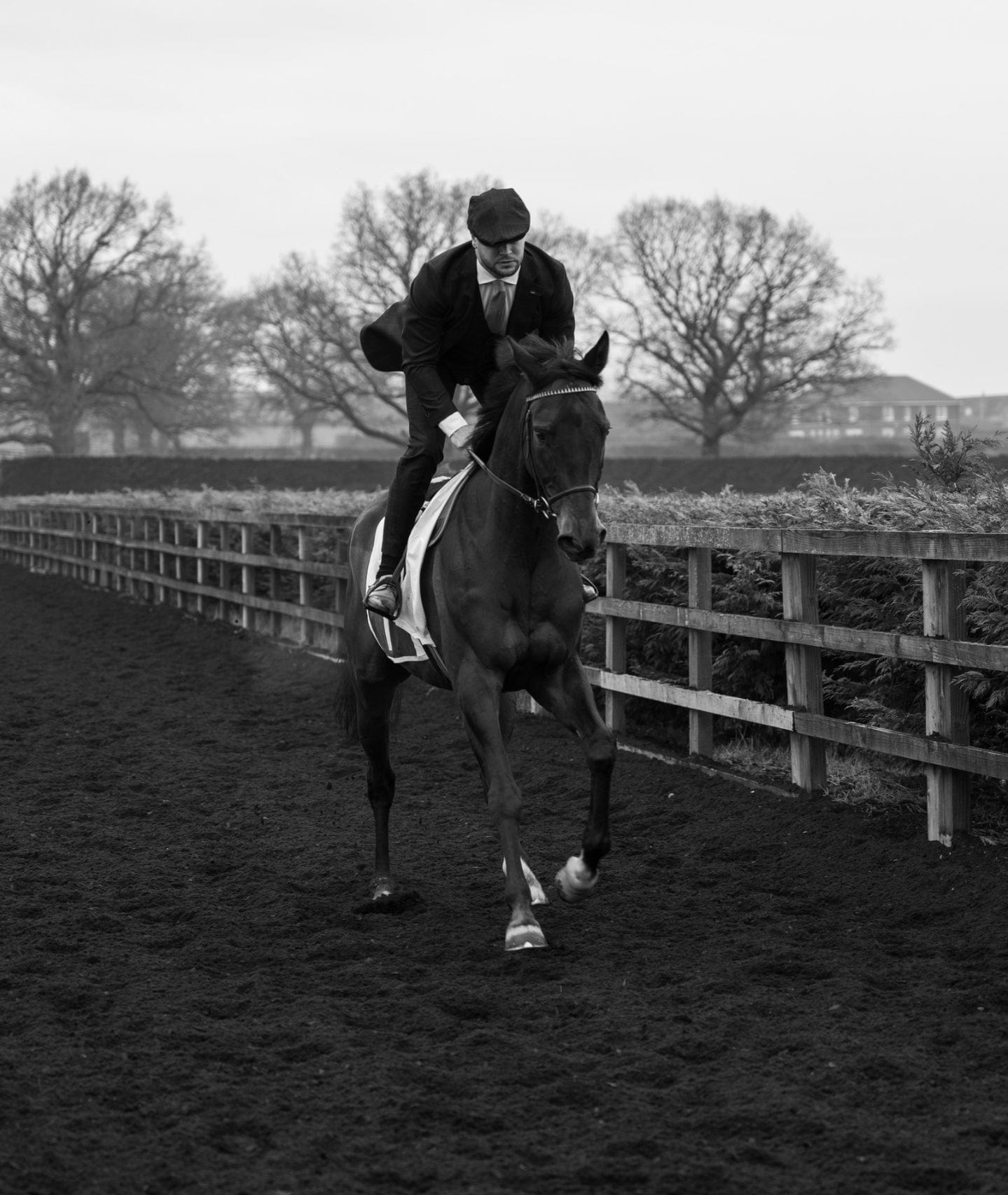 Person riding a horse on a track with trees and a building in the background