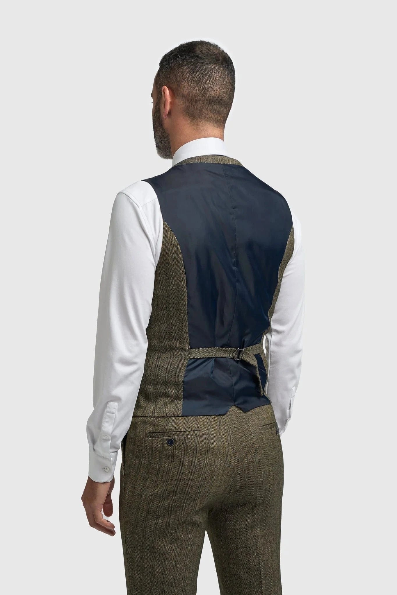 Man wearing a navy vest over a white shirt with brown trousers on a light gray background