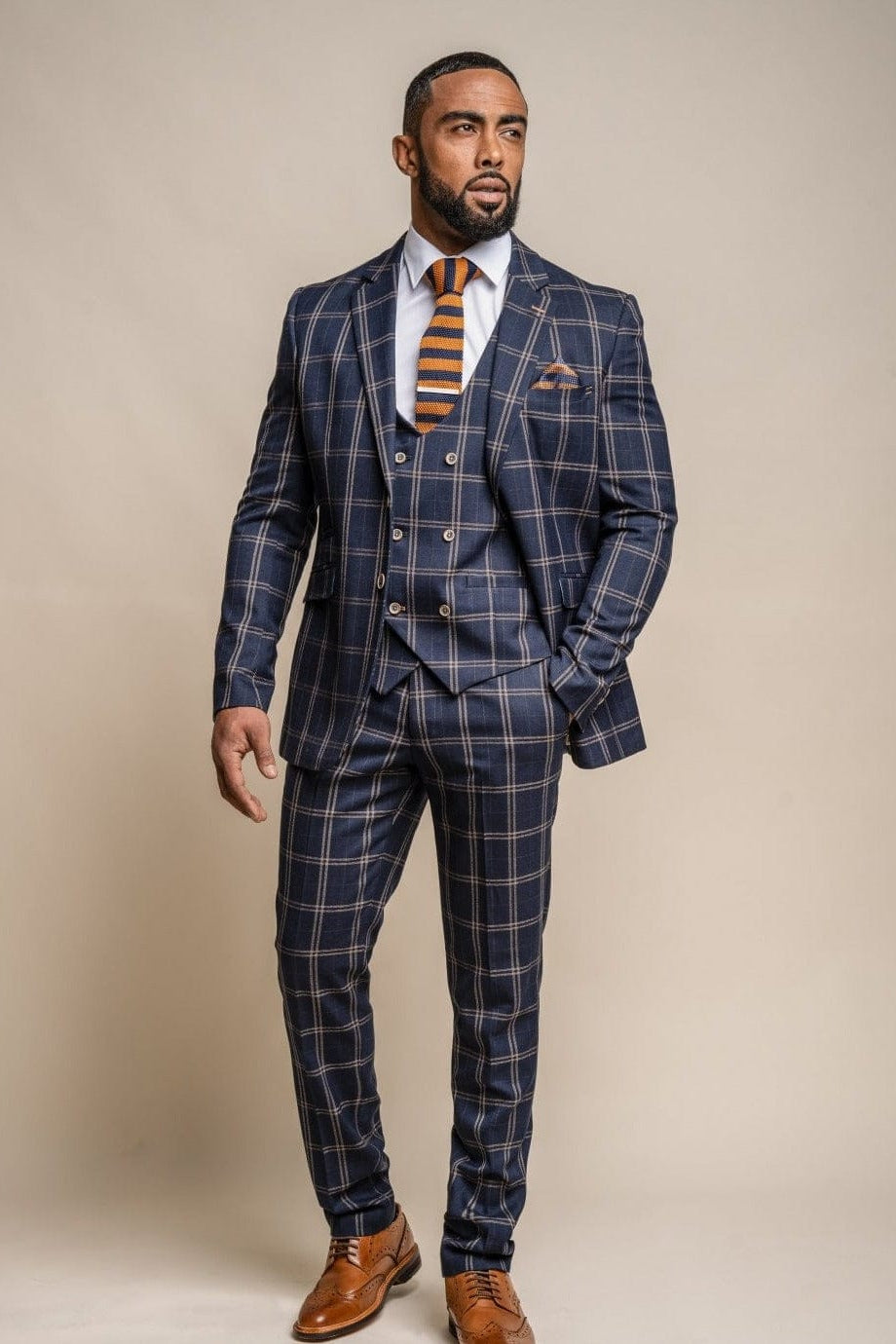 A man wearing a Cavani hardy navy check three-piece suit with a tie and brown shoes.