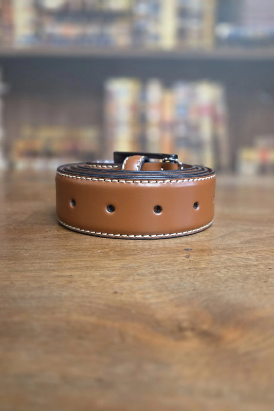 A tan leather belt with white contrast stitching and a black buckle, resting on a wooden tabletop with a blurred background.