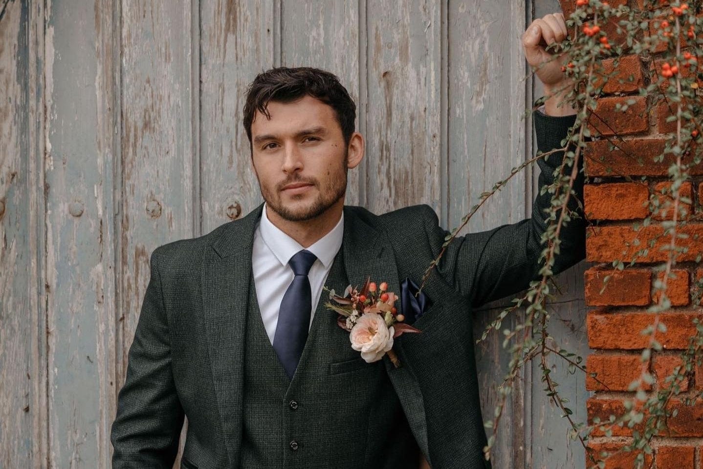 A man standing looking forward, wearing a Cavani caridi olive 3 piece suit, attending a wedding, who is one of the groomsmen.