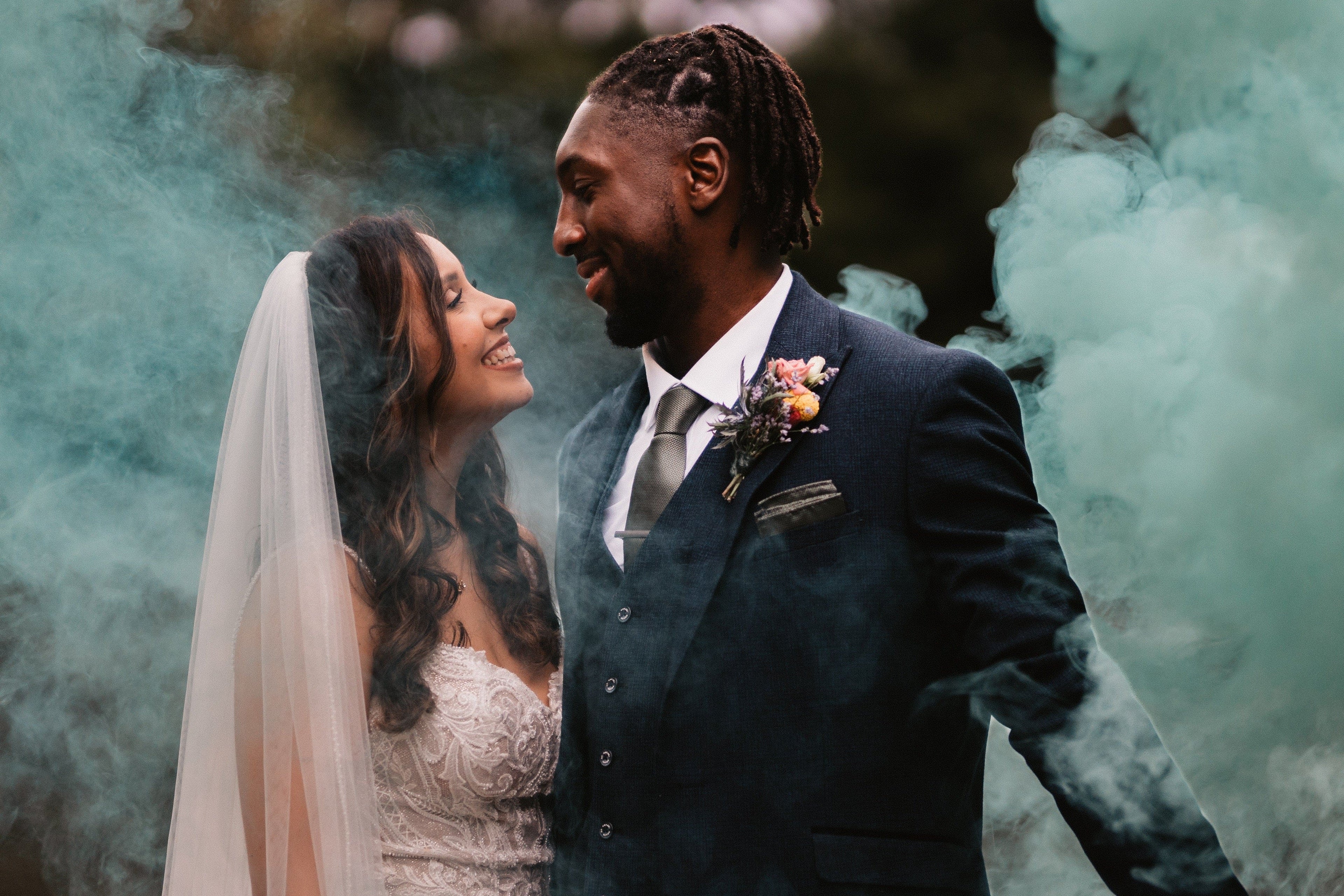 Couple in wedding attire standing amidst green smoke