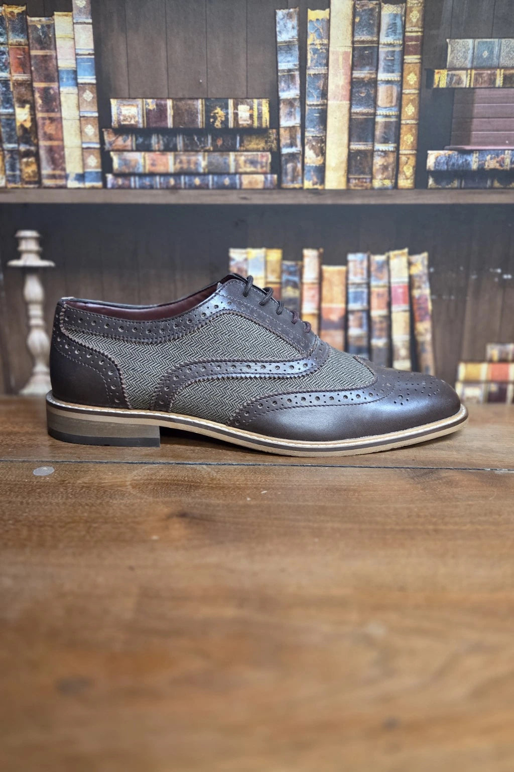 Men's Cavani Ellington Brown Brogue Shoe, positioned on a wooden table with a blurred bookshelf background.