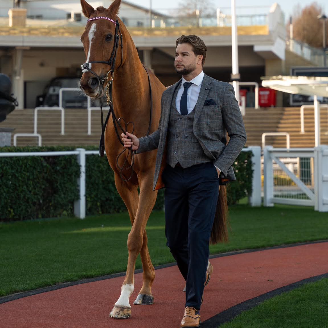 Man in formal attire walking a horse on a track