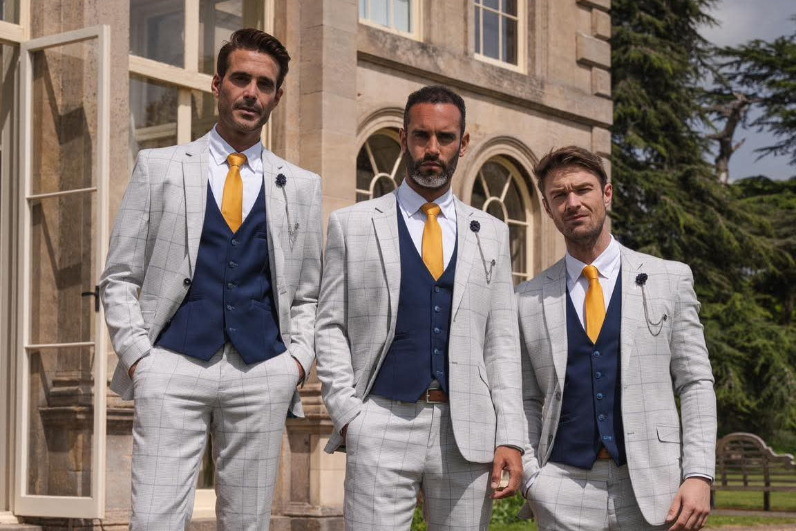 Three men in Cavani Radika light gray suits with navy vests and yellow ties standing on steps in front of a building.