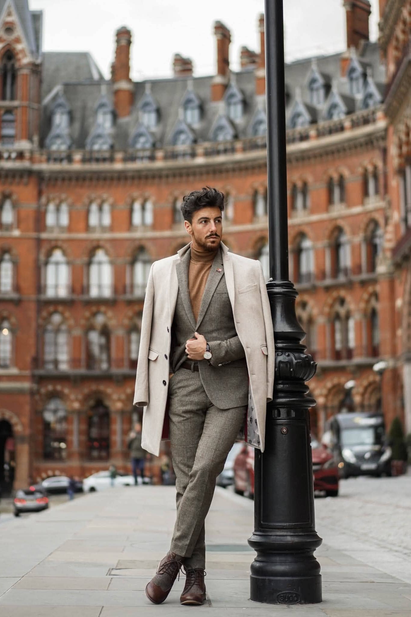 Man in a cavani Gaston sage tweed suit standing next to a lamp post with a large brick building in the background
