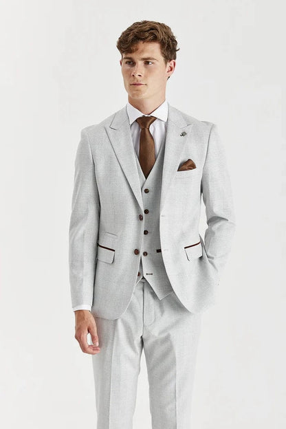 Man wearing a Paul Andrew stone check suit with a white shirt and brown shoes on a white background