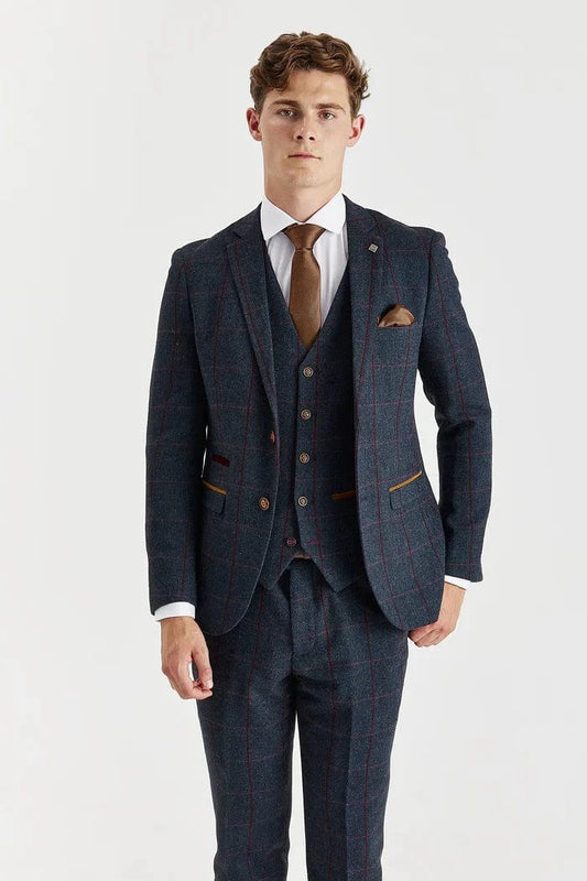 Man wearing a paul andrew navy check tweed suit with a white shirt and brown tie on a light gray background