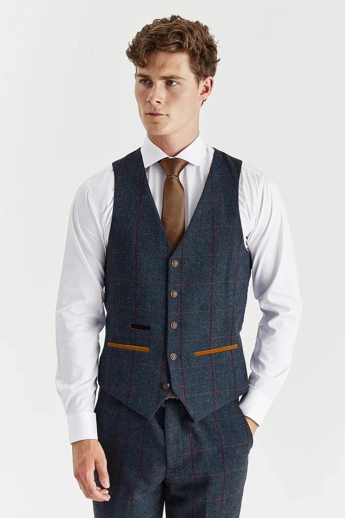 Man wearing a navy check tweed suit vest over a white shirt with a brown tie on a light gray background