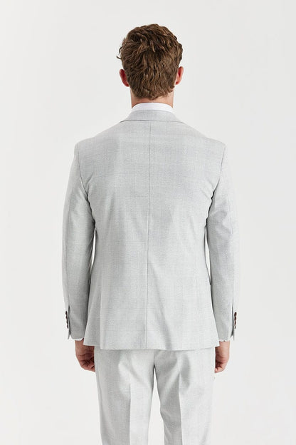 Man wearing a Paul Andrew stone check suit with a white shirt and brown shoes on a white background
