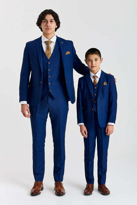 Father and Son wearing matching Paul Andrew Mayfair Blue Three Piece Suits, with brown shoes and a white bac ground