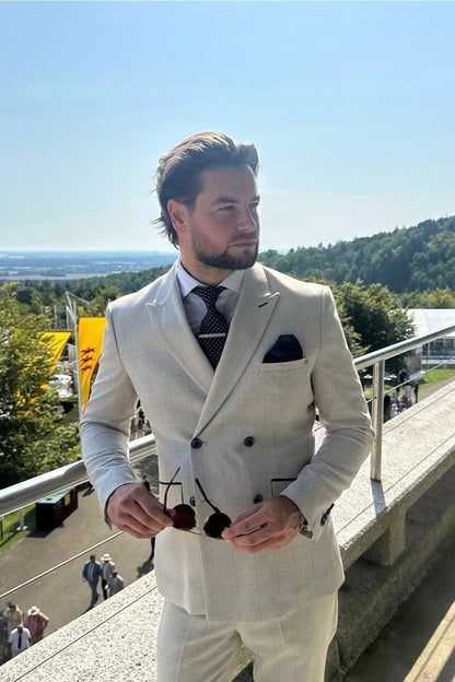 Man in a light-colored suit standing on a balcony with a scenic view.