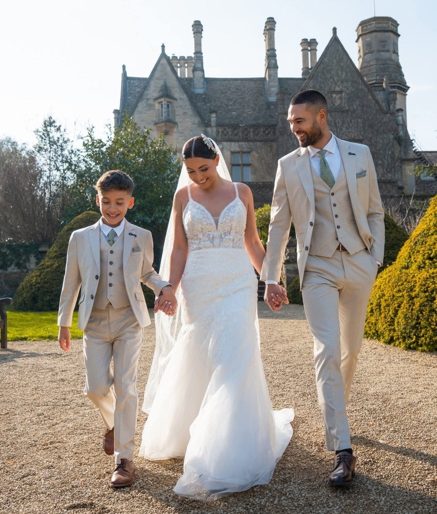 Wedding couple with a child walking in front of a large, ornate building.