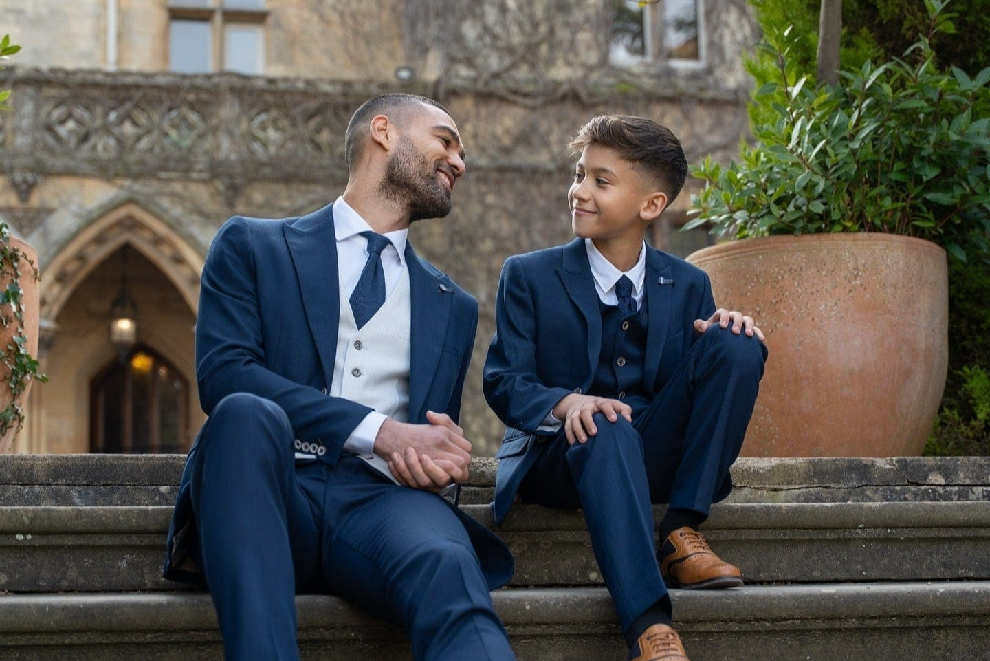 Two men in formal suits sitting on steps in front of an elegant building.