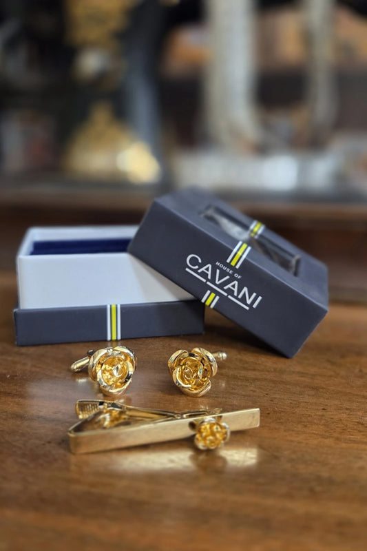 Gold-tone rose-shaped cufflinks and a matching tie bar set with branded navy Cavani gift boxes on a wooden surface.