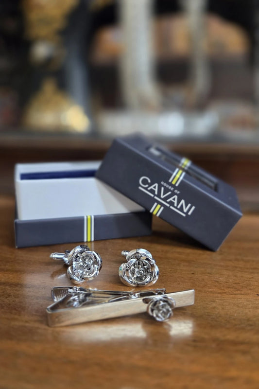 Silver-tone rose-shaped cufflinks and matching tie bar set on a wooden table, with the open presentation box and branded dark navy Cavani box behind them.