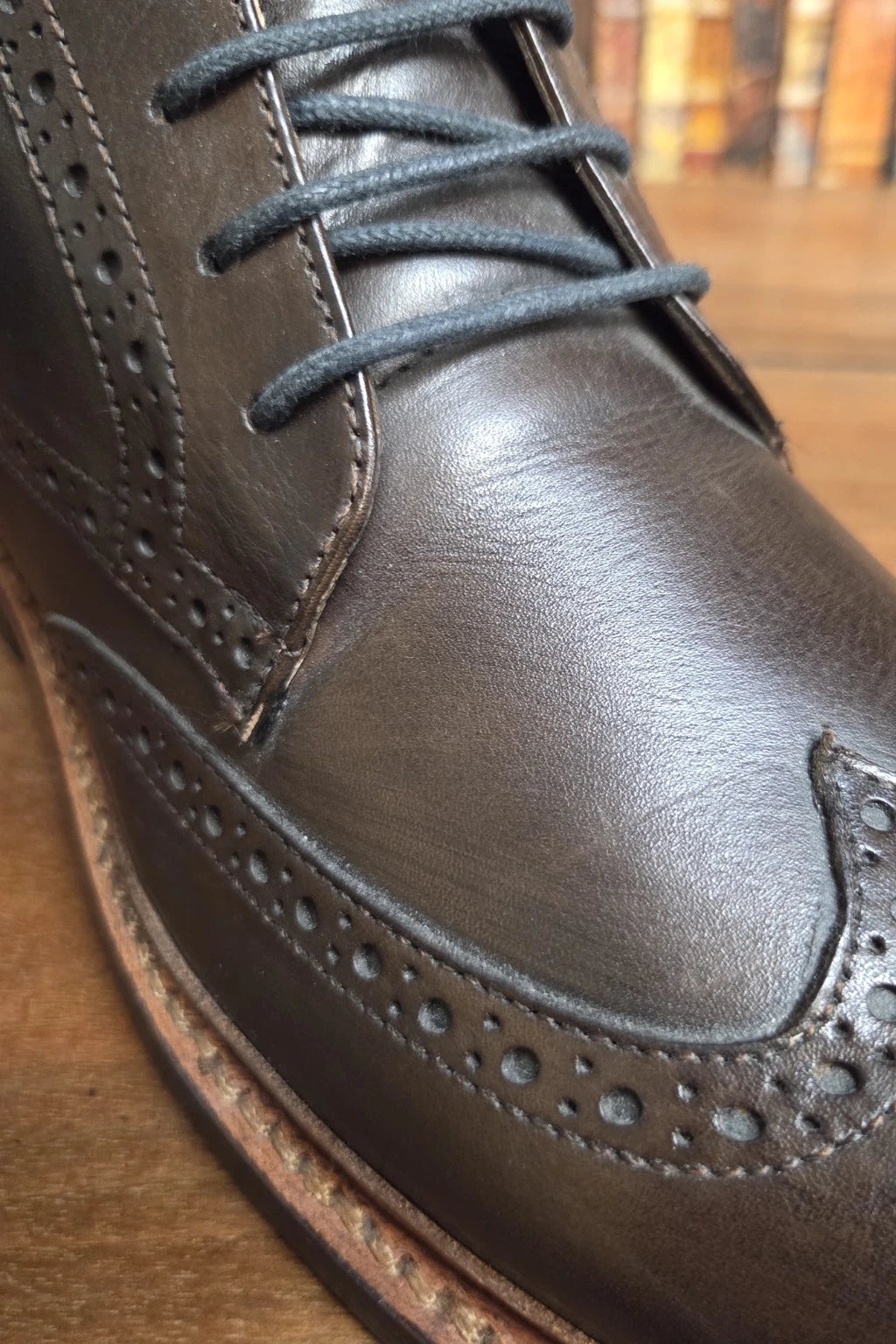 A close-up shot of a dark brown leather wingtip brogue shoe with dark gray laces, resting on a wooden surface.