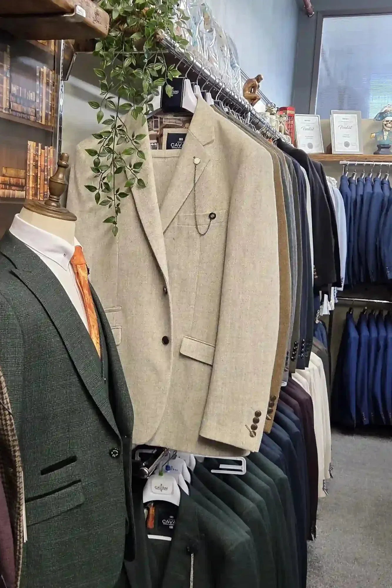 Inside Menz Suits Stockport with three mannequins displaying tweed and formal three-piece suits alongside overcoats and accessories.